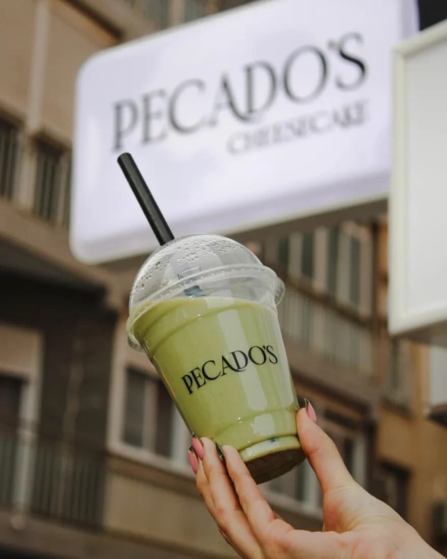 Un matcha latte de Pecados en la mano, delante del cartel de la tienda